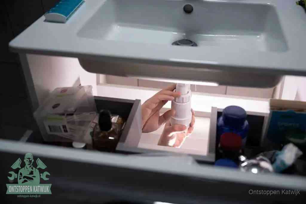 Een pompfles met zeep boven een wastafel, de heet water en afwasmiddel-methode om een vetprop in de afvoer los te maken in Katwijk