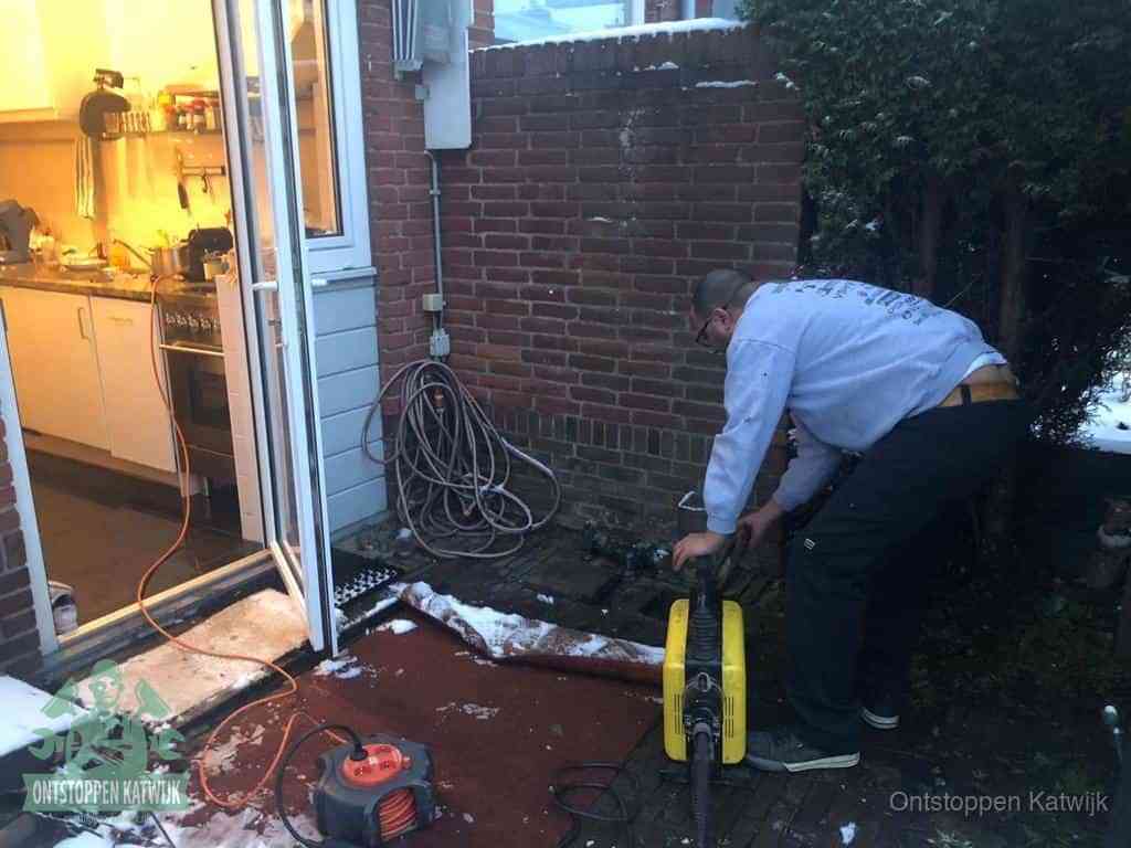 Een monteur werkt buiten bij een open riool-/grondput met een elektrische ontstoppingsmachine om een verborgen afvoerprobleem op te sporen in Katwijk
