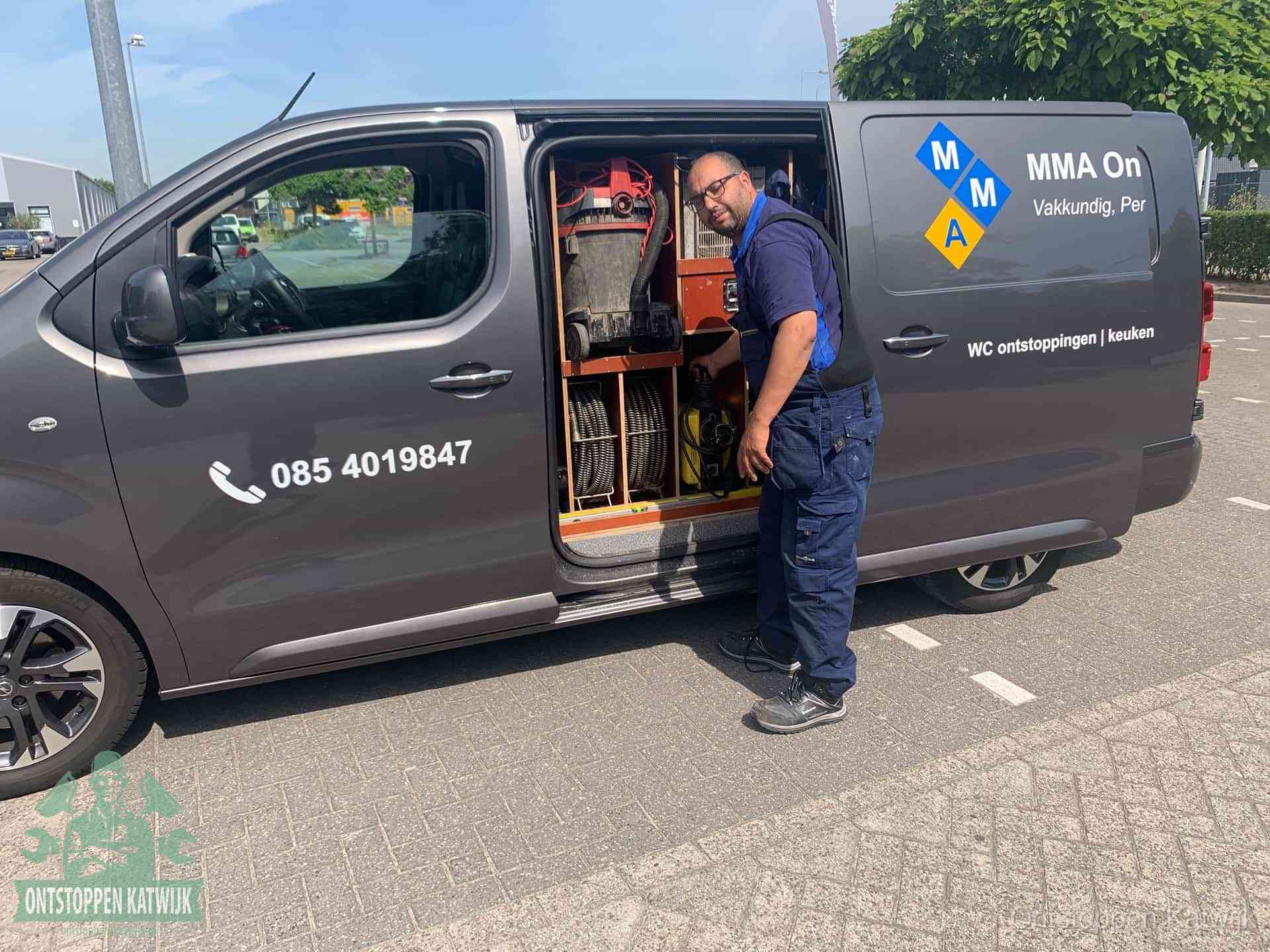 Een monteur bij de open schuifdeur van zijn bedrijfsbus op een parkeerplaats, klaar om de oorzaak van terugkerende afvoerverstoppingen aan te pakken in Katwijk