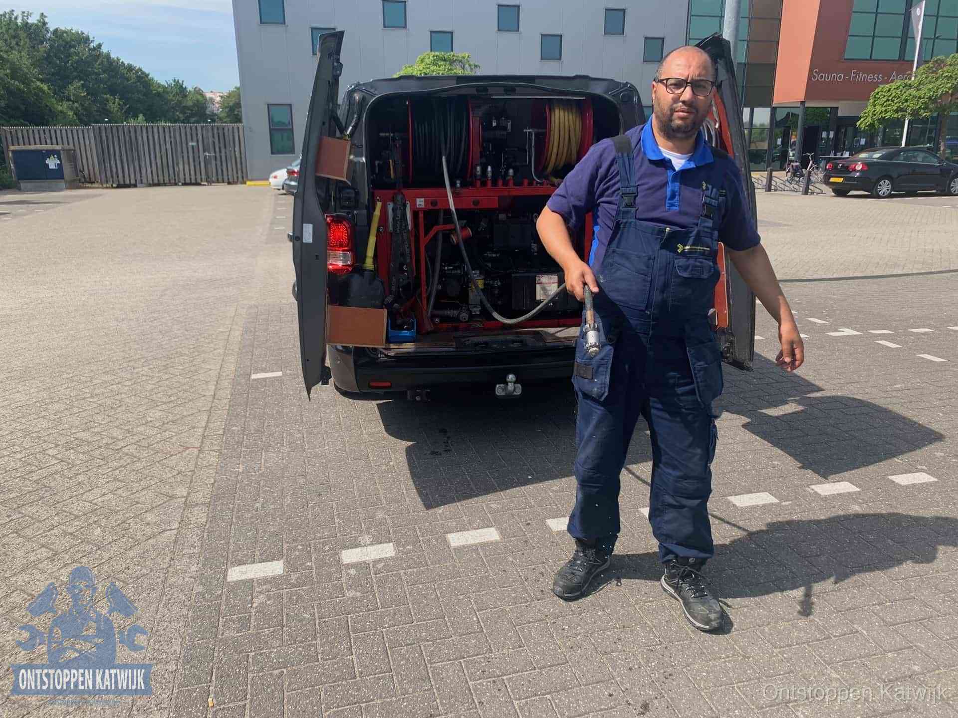 Een monteur bij zijn bestelbus met een hogedruk- en rioolreinigingsunit, klaar om de oorzaak van terugkerende wc-verstoppingen aan te pakken in Katwijk