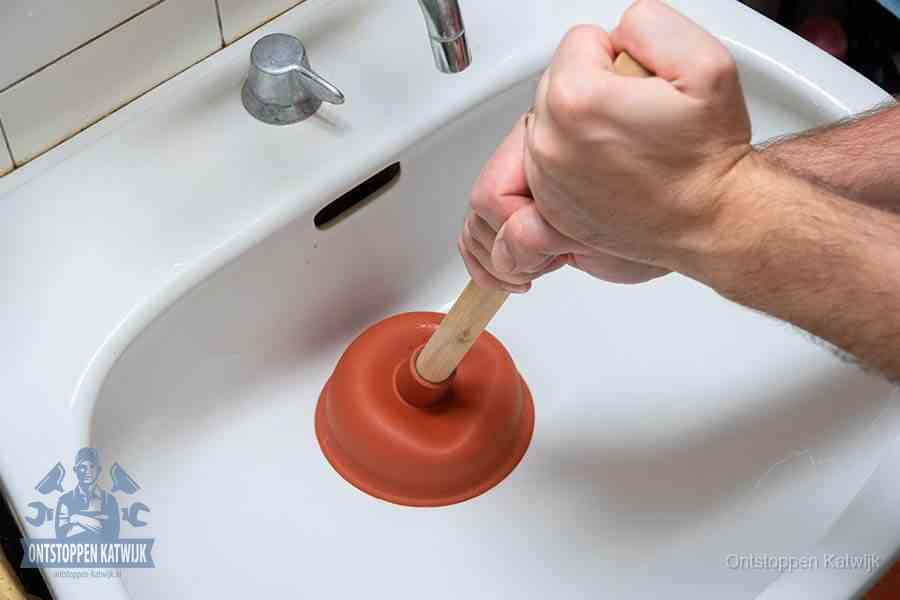 Twee handen gebruiken een rode rubberen plopper op een sanitair-afvoer om het toilet te ontstoppen in Katwijk