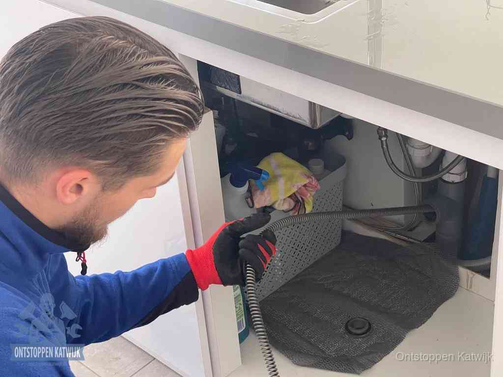 Een monteur voert een flexibele ontstoppingsveer in de afvoer om een verstopping voorbij de bocht van het toilet te bereiken in Katwijk