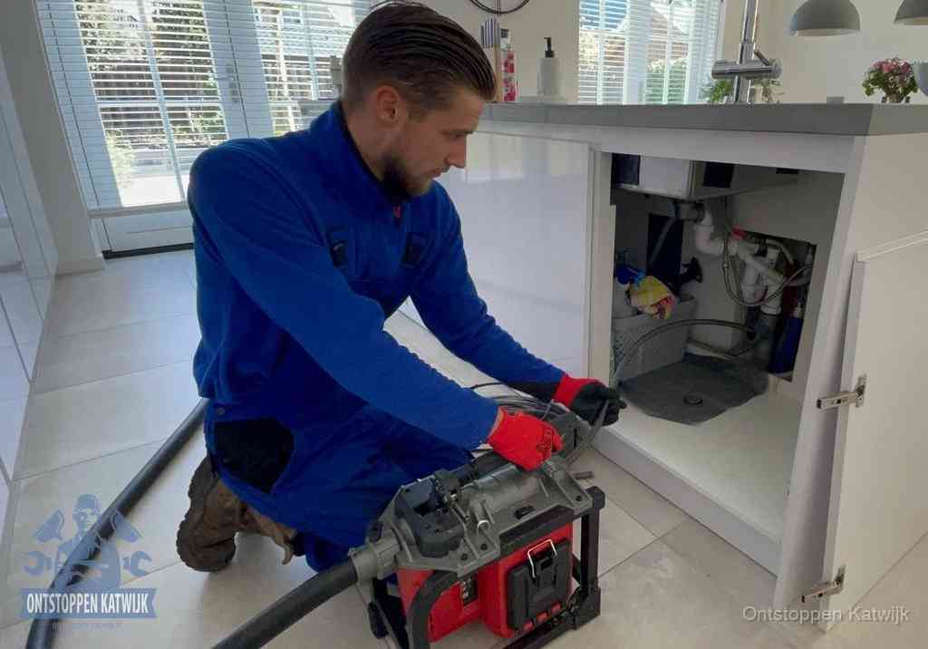 Een monteur voert een professionele elektrische ontstoppingsmachine in de afvoer onder de spoelbak tijdens het gootsteen ontstoppen in Katwijk