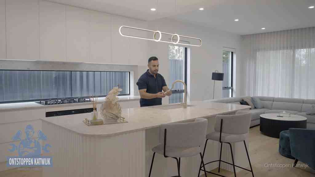 Een bewoner bij de keukenspoelbak die zelf aan de slag gaat met een verstopte gootsteen in Katwijk